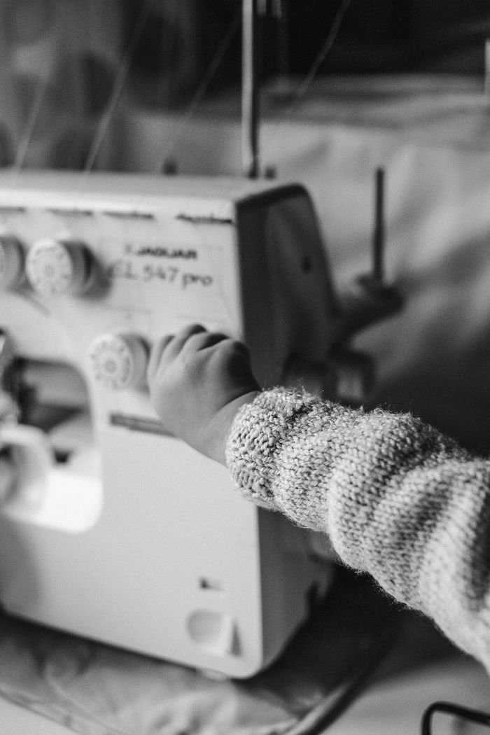 A childs hand interacts with a sewing machine in a black and white setting.